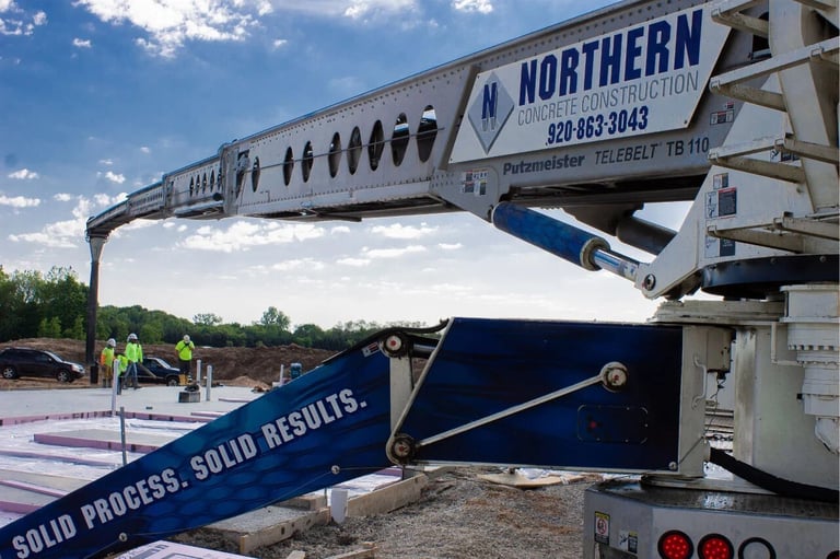 Northern concrete pump truck with extended boom positioned at construction site, workers in safety vests visible in background.